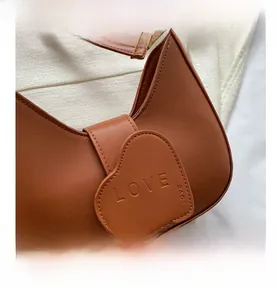 Dettaglio borsa a mezzaluna color caramello con patta a cuore e incisione LOVE