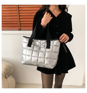 Close-up of quilted silver metallic tote bag featuring wide black shoulder straps and padded texture