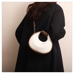 Detail of white woven crescent bag with brown leather trim worn by a model