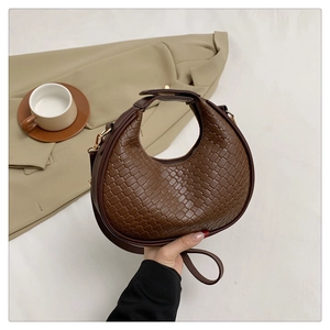 Close-up of dark brown woven crescent bag with leather handle and golden hardware
