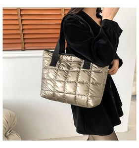 Champagne metallic quilted tote bag with black strap worn over the shoulder by a model