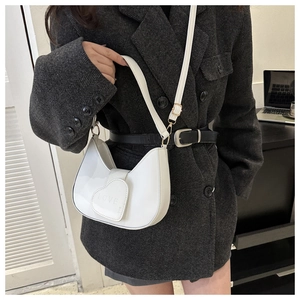 Close-up of a white heart-shaped flap bag with 'LOVE' engraving worn with a grey blazer