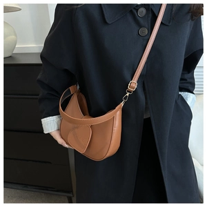 Dettaglio borsa a mezzaluna marrone con patch a cuore e fibbie dorate su cappotto nero