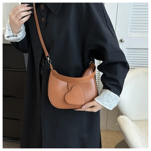 Dettaglio borsa a mezzaluna marrone con toppa a cuore love indossata su cappotto nero