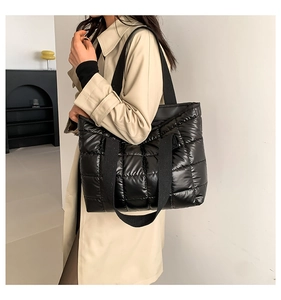 Detailed view of a black puffer tote bag with quilted pattern on a beige trench coat