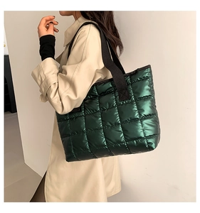 Detail of green glossy quilted tote bag with wide black strap and metallic nylon finish