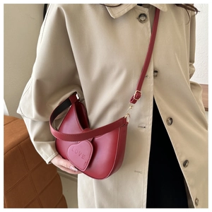 Detail of red PU leather bag featuring a heart charm with LOVE engraving and crossbody strap