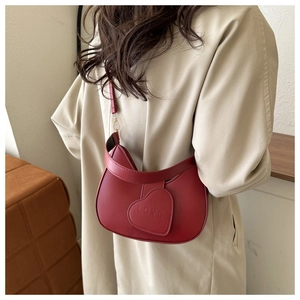 Detail of red half-moon shoulder bag with love heart tag on a beige trench coat