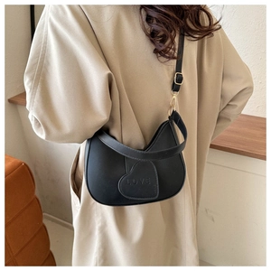 Chic black hobo bag with LOVE heart patch worn over a stylish beige trench coat
