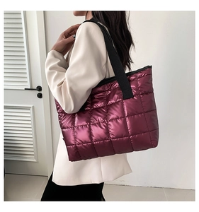 Close-up of metallic burgundy quilted tote bag with wide black strap on female model