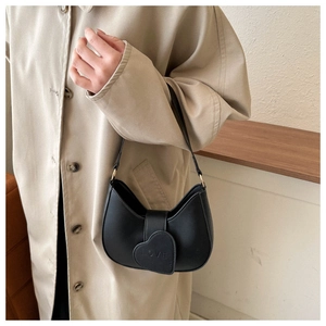 Close-up of black heart-shaped hobo bag with LOVE embossed detail on a trench coat