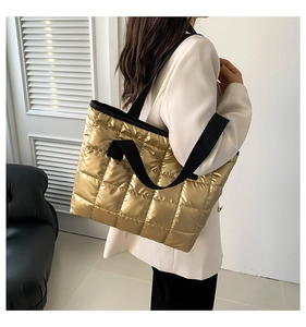 Detail of metallic gold quilted tote bag with black wide straps in minimalist setting