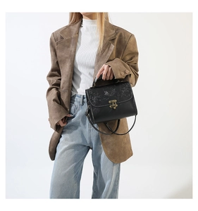 Detail of vintage embossed floral pattern on black leather crossbody bag with bronze clasp