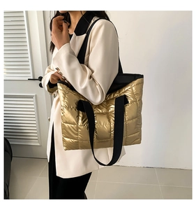 Close-up of golden quilted tote bag with metallic finish and black canvas shoulder strap