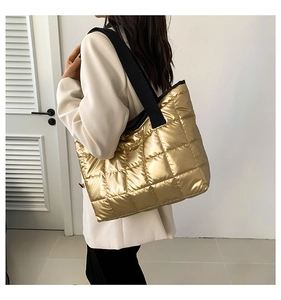 Detail of gold quilted puffer tote bag featuring glossy finish and wide black strap
