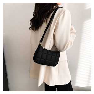 Minimalistische schwarze gesteppte Filz-Schultertasche über weißem Blazer getragen