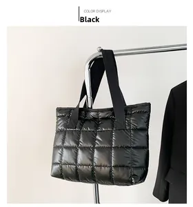 Detail of black quilted puffer tote bag with wide strap handles and glossy nylon texture