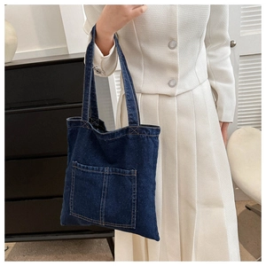 Detail of a large dark blue denim tote bag with external pockets worn by a model
