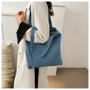 Blue denim tote bag with front pockets shown on model for size and style reference