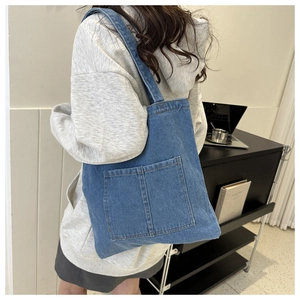 Rear view of a casual blue denim tote bag with two front pockets worn by a model