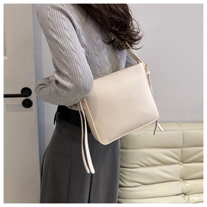 Borsa a tracolla crema minimalista con ampia tracolla su un maglione grigio lavorato