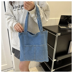 Close-up of blue denim tote bag featuring dual front pockets and durable shoulder straps