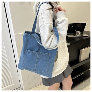 Casual blue denim tote bag with two front pockets worn over the shoulder by a model