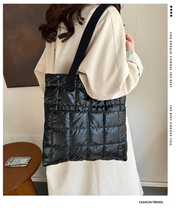 Close-up of black quilted down tote bag with glossy texture and wide fabric shoulder strap
