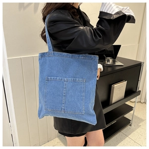 Detailed view of blue denim tote bag featuring two front pockets and durable stitching