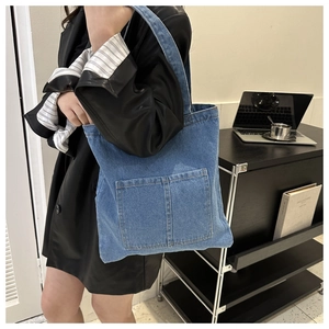 Detail of blue denim tote bag with functional front pockets and wide shoulder strap
