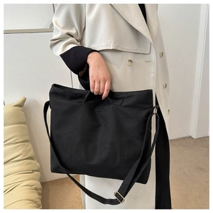 Détail du grand sac cabas en toile noire avec poignées et bandoulière sur un mannequin