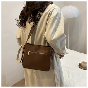Dettaglio borsa a tracolla in pelle marrone con ampia tracolla jacquard e tasca con zip