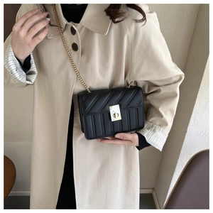 Chic black quilted crossbody bag with gold chain strap worn over a beige trench coat