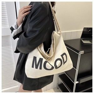 Vue latérale d'un sac cabas en toile crème avec lettrage MOOD sur un blazer noir
