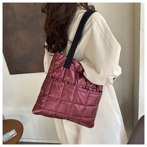 Side view of a wine red quilted down tote bag with metallic nylon finish on a model