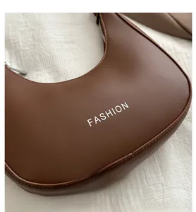 Detail view of brown half-moon underarm bag with white FASHION print and silver zipper