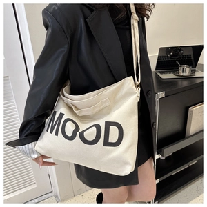 Détail du sac cabas en toile beige avec imprimé MOOD porté sur un blazer en cuir noir