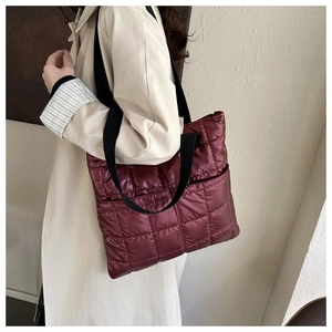 Close-up of wine red quilted tote bag with black strap worn over the shoulder