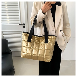 Golden quilted down tote bag with black straps in a minimalist indoor setting