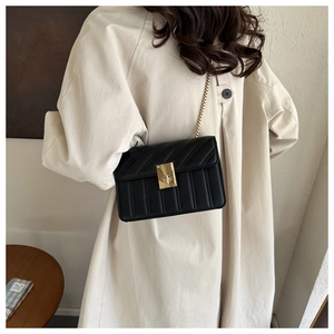 Detail of black quilted leather shoulder bag with gold chain strap on beige coat
