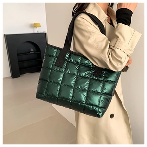 Deep green quilted tote bag with metallic finish and black wide straps on model