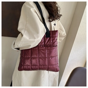 Close-up of quilted puffer tote bag in deep red featuring black straps on a trench coat