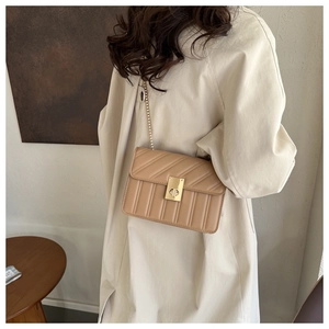 Close-up of beige quilted crossbody bag featuring a golden chain and metal twist lock