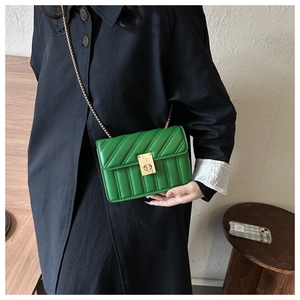 Green quilted chain small square bag worn over a black trench coat for a stylish look