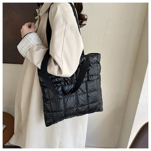 Close-up of black quilted puffer tote bag with wide strap on a model's shoulder