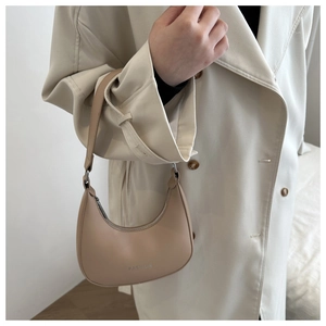 Detail of the cream-colored crescent hobo bag worn with a classic autumn trench coat