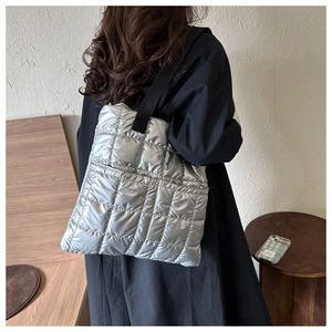 Detail view of silver quilted down fabric tote bag with black strap on casual outfit
