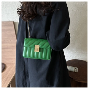 Detail of green quilted crossbody bag with gold chain strap worn over a black coat