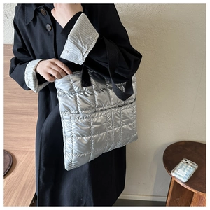 Detail of silver quilted puffer tote bag with black strap and metallic finish texture