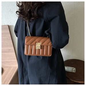 Brown quilted chain shoulder bag with gold twist lock worn by a model in a black trench coat